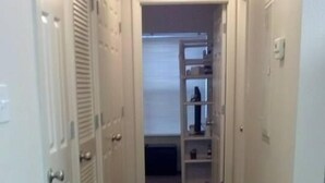 Un couloir étroit, doté d’un plancher en bois, mène à un espace de rangement avec des étagères et un radiateur.