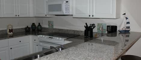 A kitchen with white cabinets, a microwave, a stove, and a granite countertop.
