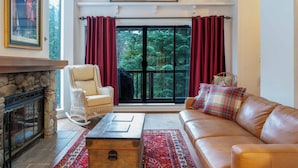Ein Wohnzimmer mit Kamin aus Stein, einer Ledersofa, einem Korbstuhl und einem großen Fenster mit roten Vorhängen.
