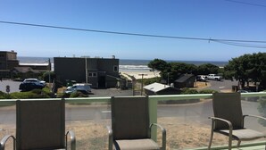 A balcony with three chairs overlooking a beach, a parking area with cars, and buildings in the background. - Sue's Dream with Beautiful Ocean Views (Florence)