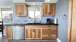 A kitchen with wooden cabinets, a black countertop, a dishwasher, and a coffee maker. - Sue's Dream with Beautiful Ocean Views (Florence)