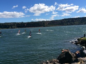 Un lac où l’on voit plusieurs pratiquants de planche à voile et une personne assise sur des rochers.