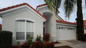 Einbungalow mit Garage, großem Fenster und gepflegtem Garten mit verschiedenen Pflanzen.