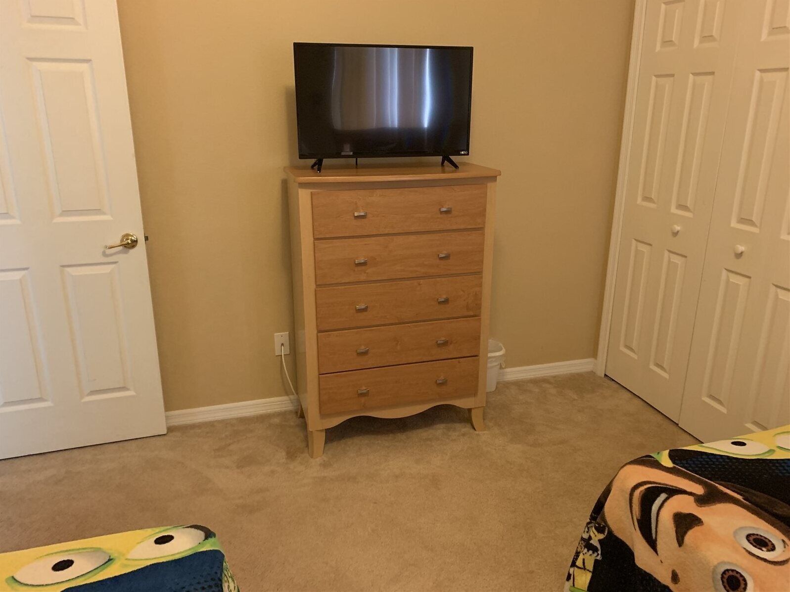 Une pièce avec une commode en bois, un téléviseur posé dessus et une porte sur le côté gauche.