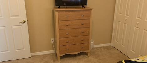Une pièce avec une commode en bois, un téléviseur posé dessus et une porte sur le côté gauche.