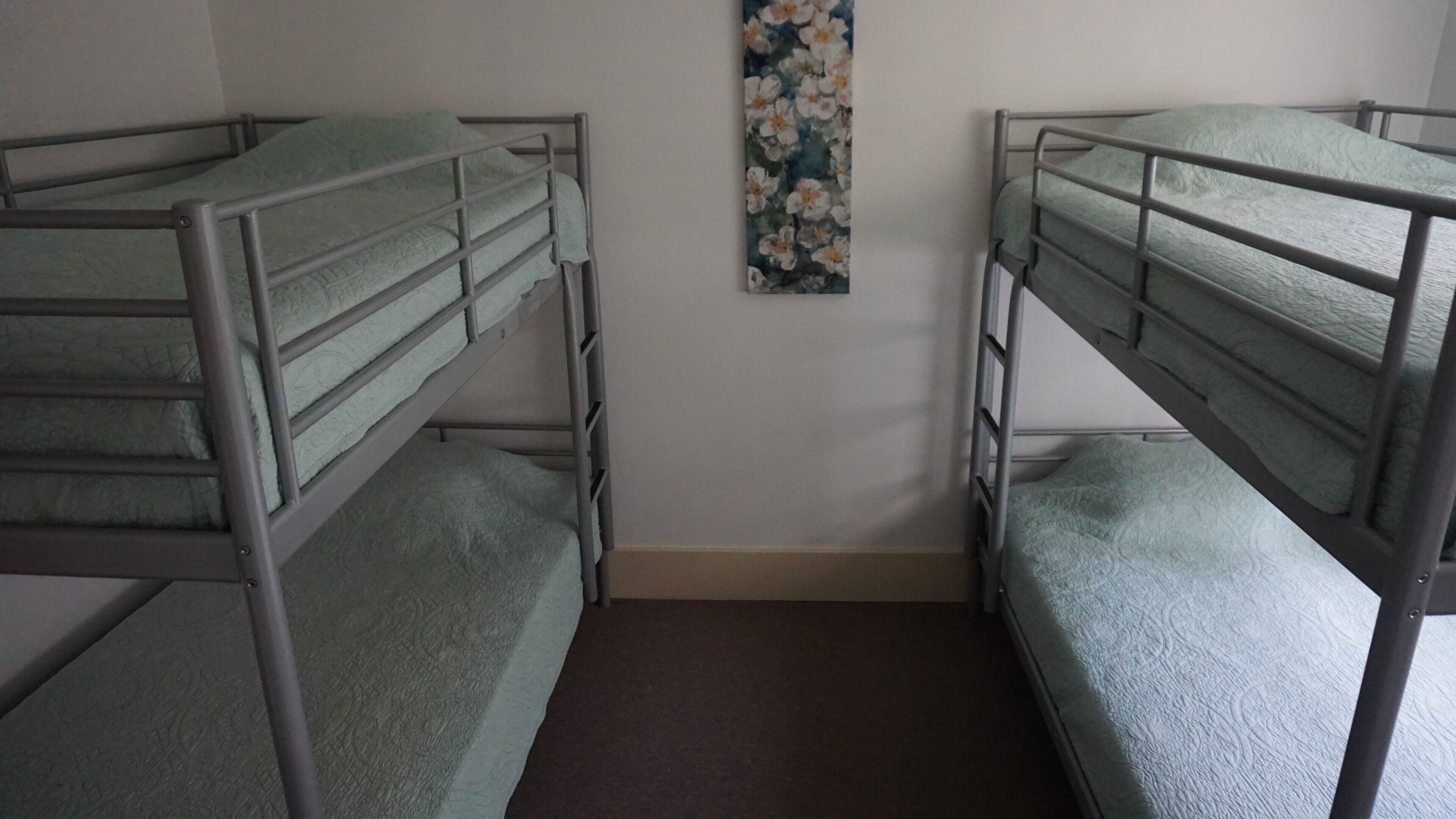 Two bunk beds with metal railings and green bedding, a brown carpeted floor, and a floral painting on the wall.