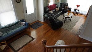 Ein Wohnzimmer mit einer Couch, einem schwarzen Ledersessel, einem kleinen runden Tisch mit einer Vase und einer Holztreppe.