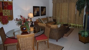 A living room with a round glass table, wicker chairs, a sofa, and a ceiling fan. - Playa Royal Oceanfront Condo (nuevo, vallarta)