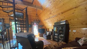 A cozy log cabin interior with a spiral staircase, a leather sofa, a wooden cabinet, and a television.