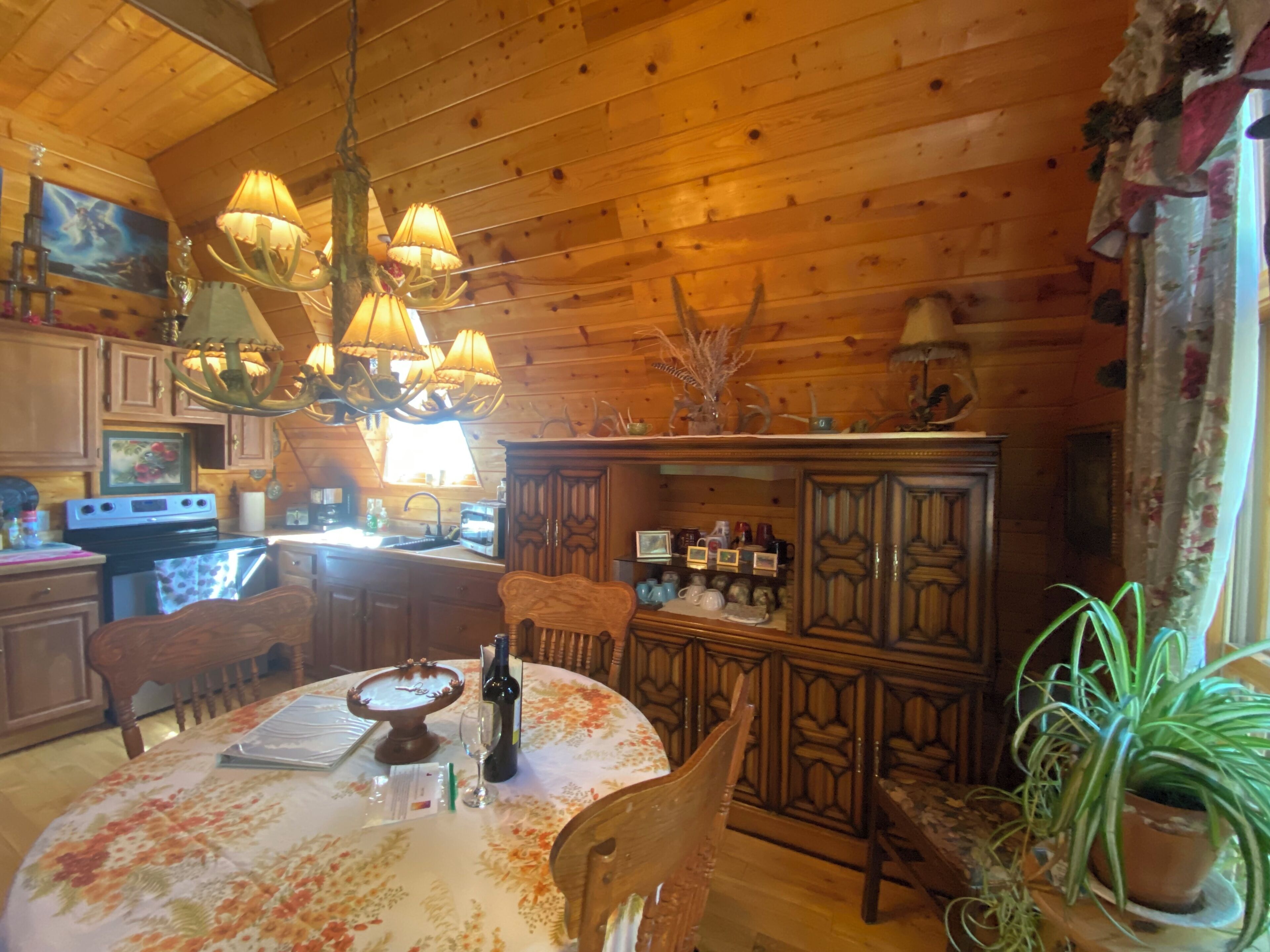 Ein Holzblockhaus-Innenraum mit Esstisch, Stühlen, einer Chandelieber und einer Küchenzeile mit Schränken und Geräten.