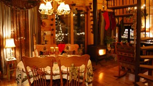 A cozy dining area with wooden furniture, a chandelier, and a Christmas tree in the background.