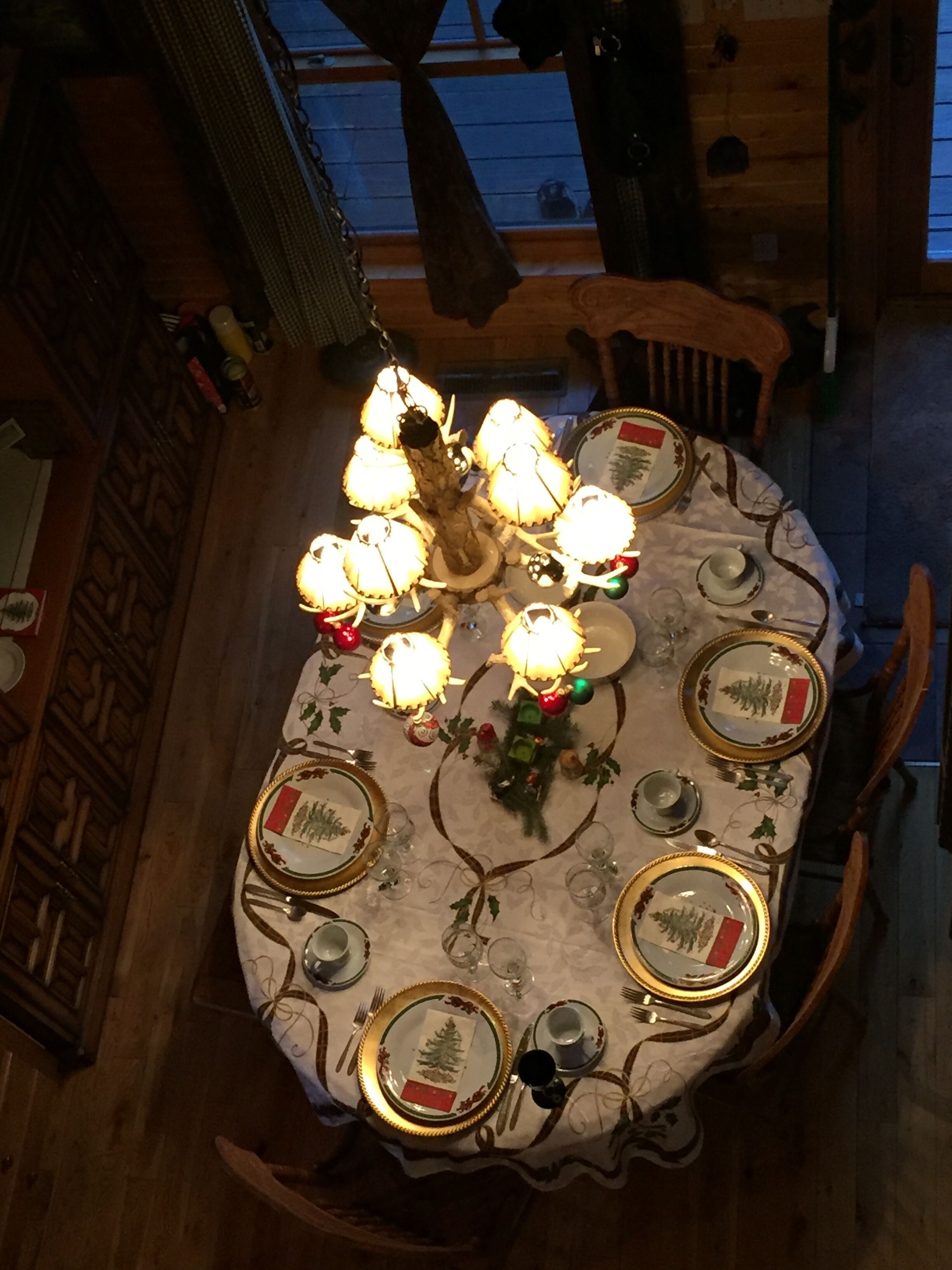 A dining table set for a meal with a chandelier above, surrounded by wooden chairs.
