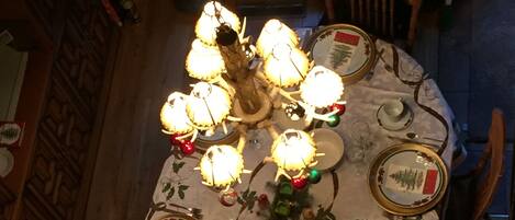 A dining table set for a meal with a chandelier above, surrounded by wooden chairs.
