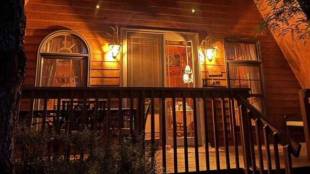 A wooden cabin with a porch, large windows, and exterior lighting.