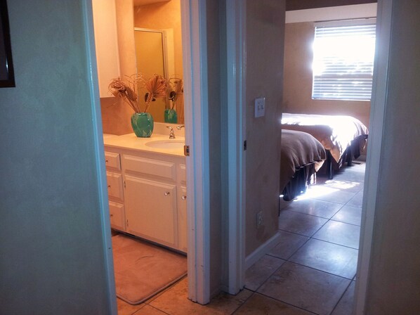 A hallway leading to a bathroom with a sink and a mirror. There is a window with blinds on the right side. - Beautiful Oceanfront Home, Gorgeous Views, Deck and Patio! Best Value! (Encinitas)