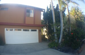 A two-story house with a white garage door, a small window on the upper floor, and a front yard with palm trees and plants. - Beautiful Oceanfront Home, Gorgeous Views, Deck and Patio! Best Value! (Encinitas)