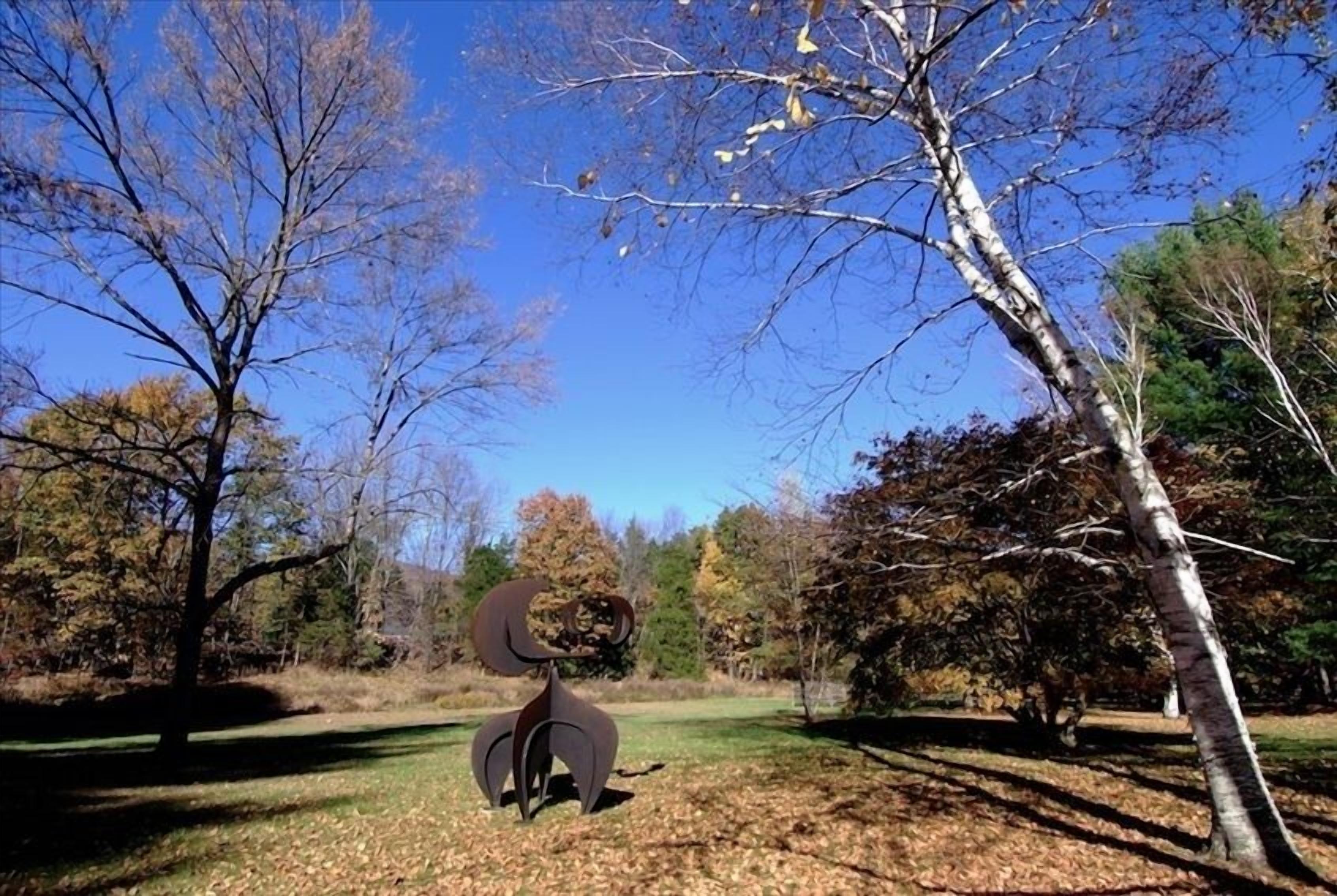 Eine Skulptur in einem Park mit Bäumen und blauem Himmel.