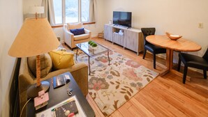 A living room with a sofa, coffee table, TV, and dining area. - Streamside Cottage Half Mile to Town of Woodstock (Woodstock)
