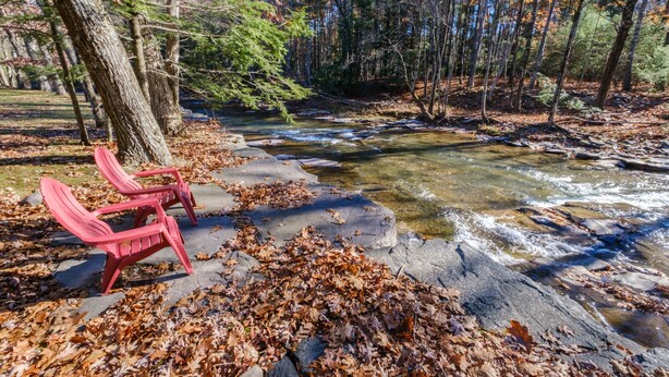 A natural setting with a stream, red chairs, and a forested area. - Streamside Cottage Half Mile to Town of Woodstock (Woodstock)