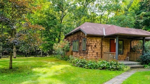 A wooden cabin with a porch, surrounded by lush greenery and trees. - Streamside Cottage Half Mile to Town of Woodstock (Woodstock)