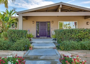A two-story house with a purple front door, a covered porch, and a well-maintained garden with various plants and flowers. - Luxury home just blocks from the magnificent El Paseo shops and restaurants (Palm Desert)