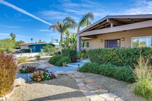 A modern house with a stone pathway leading to the entrance, surrounded by lush greenery and palm trees. - Luxury home just blocks from the magnificent El Paseo shops and restaurants (Palm Desert)
