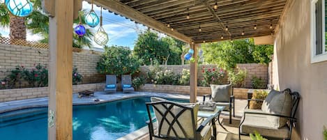 A covered outdoor area with a pool, seating, and decorative lighting.