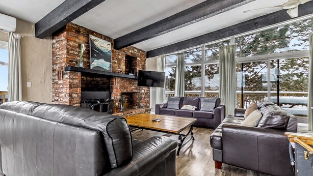 A modern living room with leather sofas, a wooden coffee table, a brick fireplace, and a large window offering a view of the outdoors. - Mountain View Blue Mountain (Blue Mountains)
