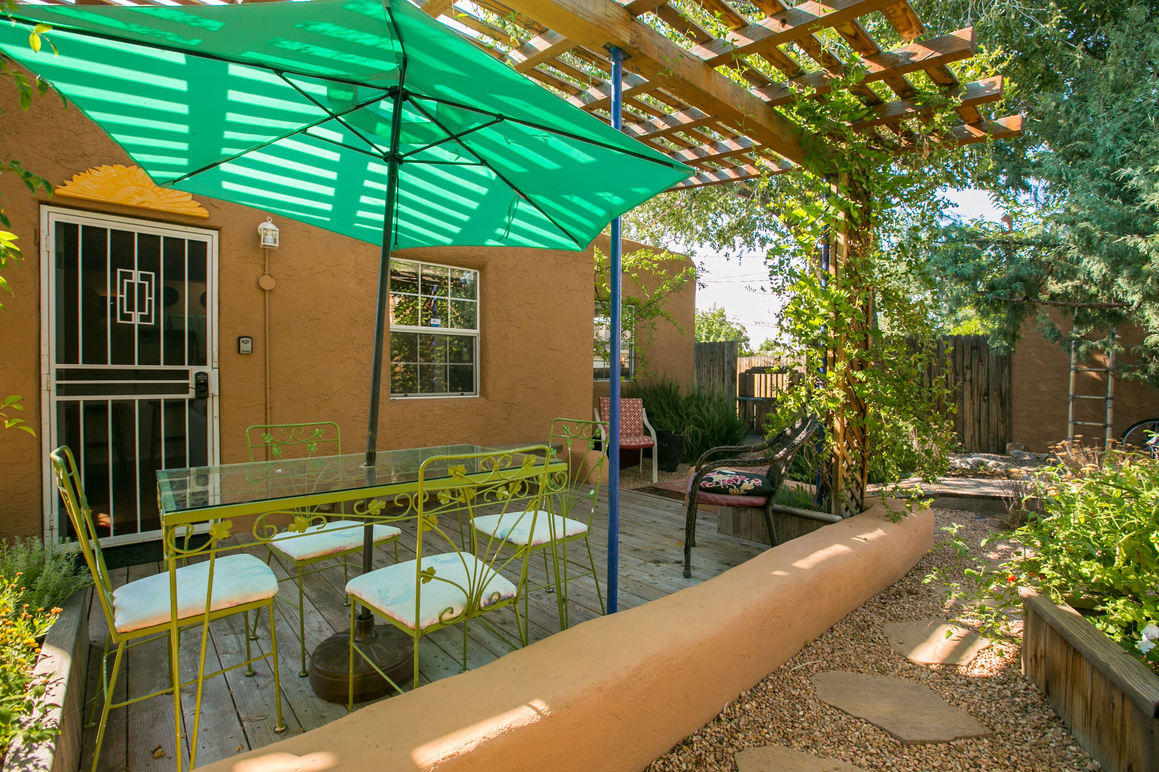 A patio with a glass table and chairs, a green umbrella, and a wooden pergola.