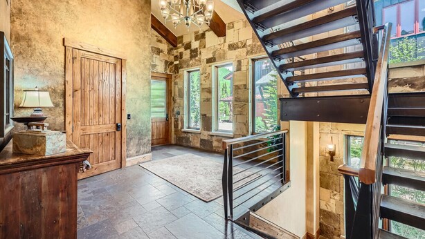 Un interior espacioso con una escalera de madera, paredes de piedra y amplias ventanas que ofrecen vistas al exterior.