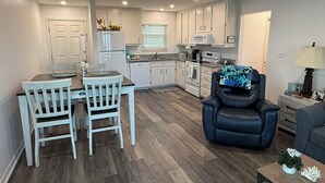 A compact kitchen with white cabinets, a dining table with two chairs, a black leather chair, and a small side table with a lamp. - SEPTEMBER BEACH TIME... NO CROWDS..LOW PRICES! (Gulf Shores)