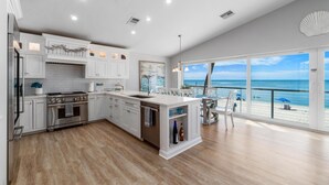 Une cuisine moderne dotée d’un grand îlot central, de meubles blancs et offrant une vue sur la plage.