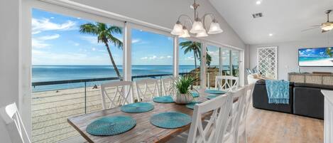 Un comedor con vistas a la playa y al océano, un ventilador de techo y un televisor en la pared.