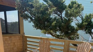 Une terrasse en bois avec des chaises Adirondack et une table, donnant sur une étendue d’eau et des arbres.