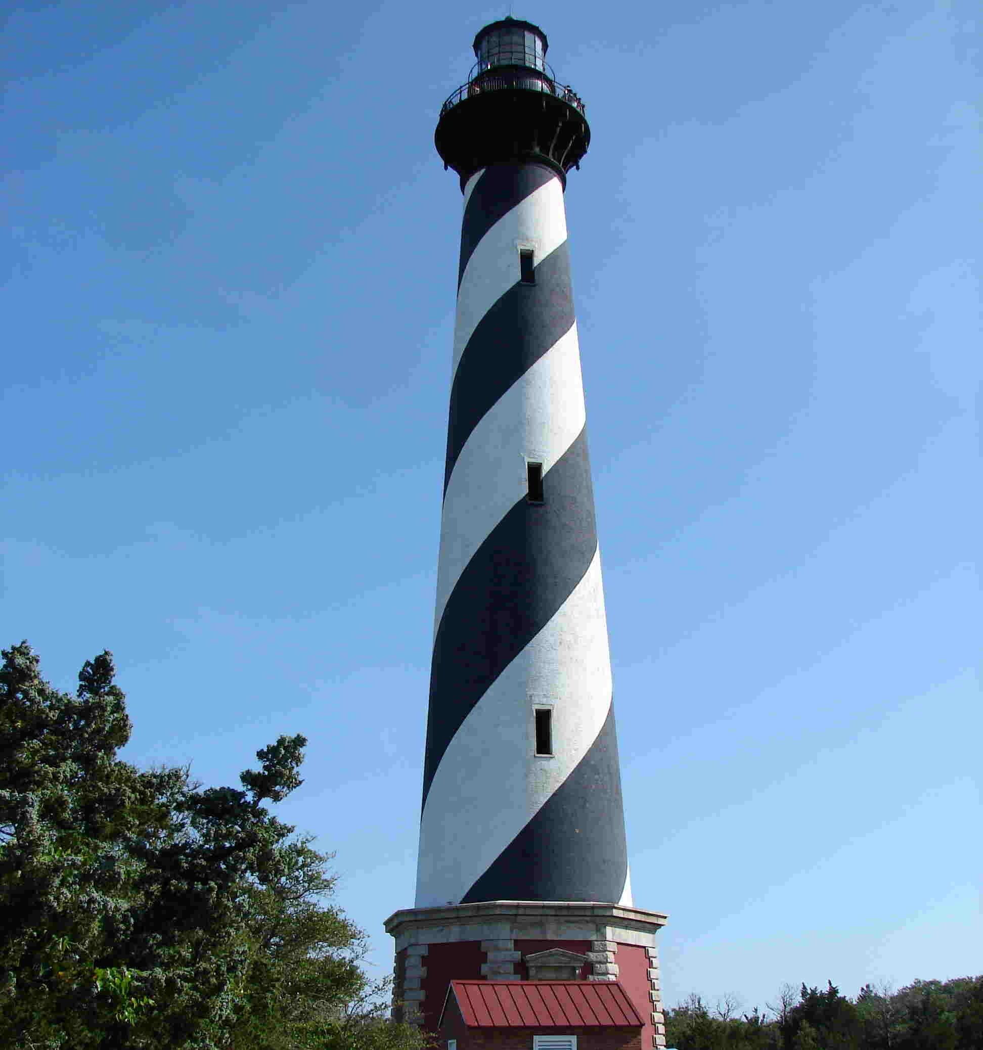 Un grand phare aux rayures noires et blanches, entouré d’arbres.