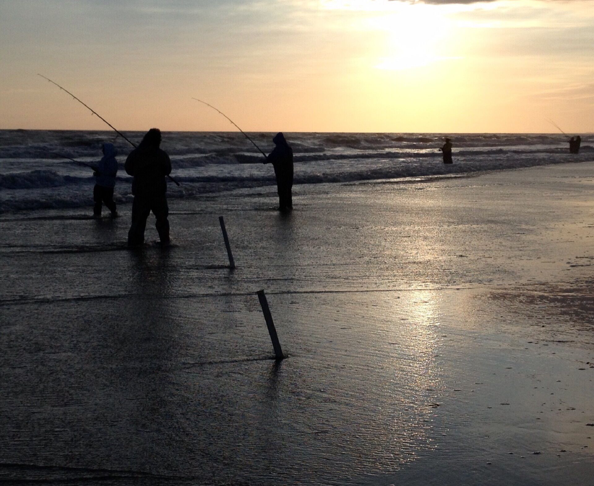 Escena de playa con gente pescando al atardecer.