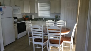 Une cuisine de taille réduite, avec des meubles blancs, une cuisinière et une table à manger entourée de quatre chaises.