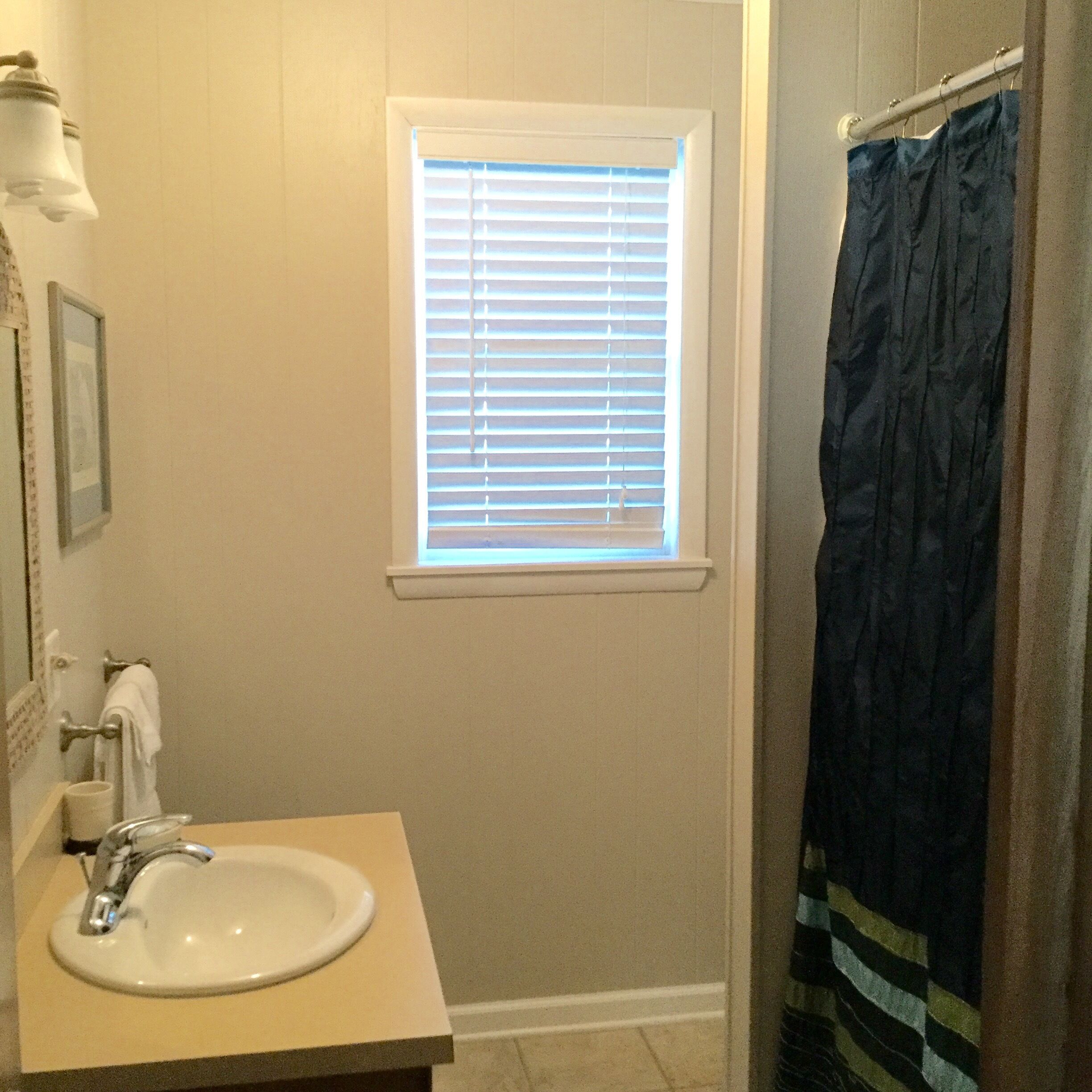 Un baño con lavamanos, ventana con persianas y cortina de ducha.