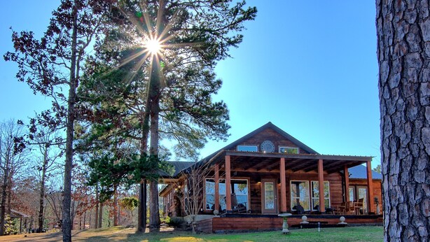 A wooden lodge with a covered porch and large windows, surrounded by trees.