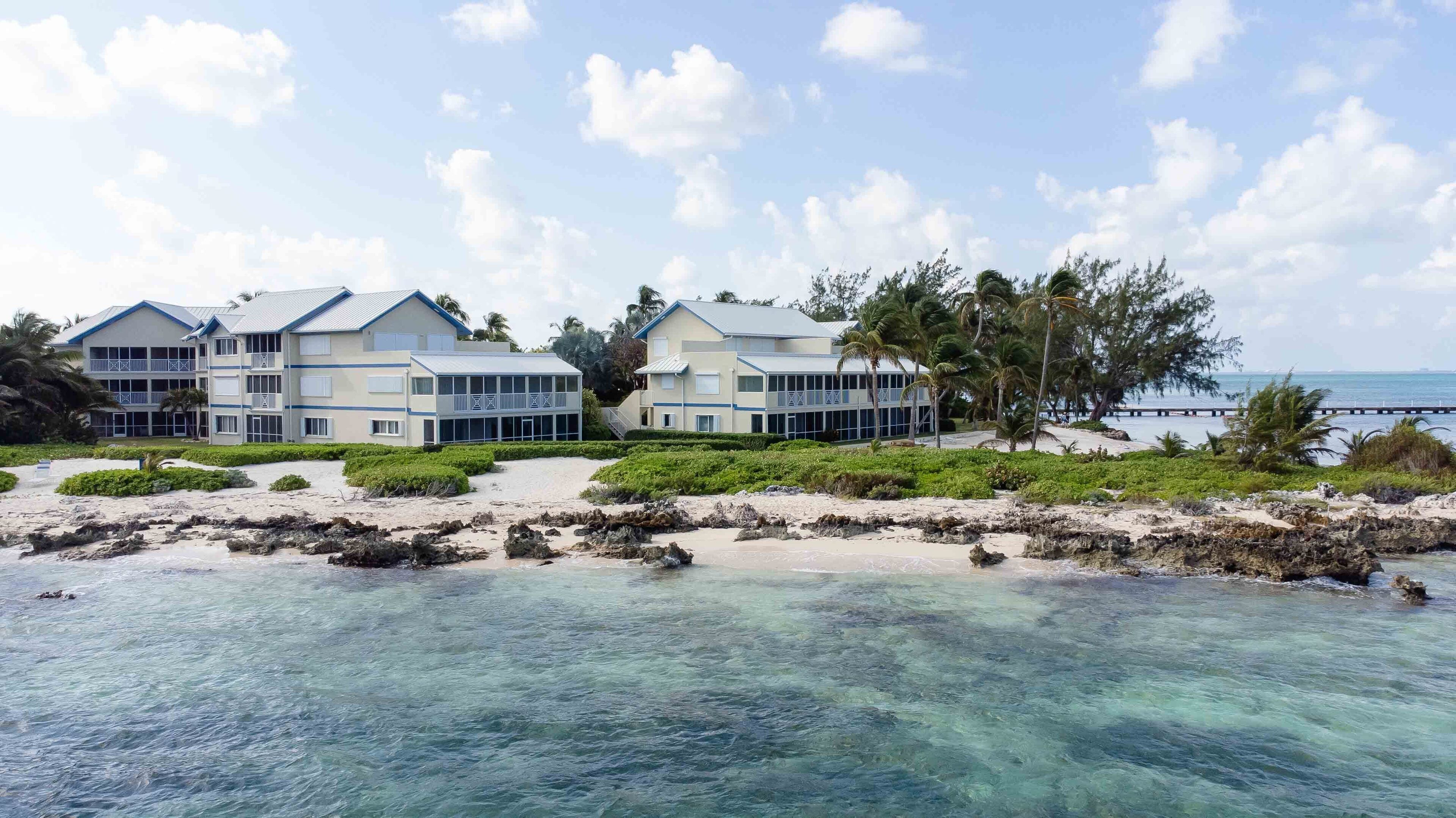 A beachfront hotel with multiple buildings, clear blue waters, and palm trees.