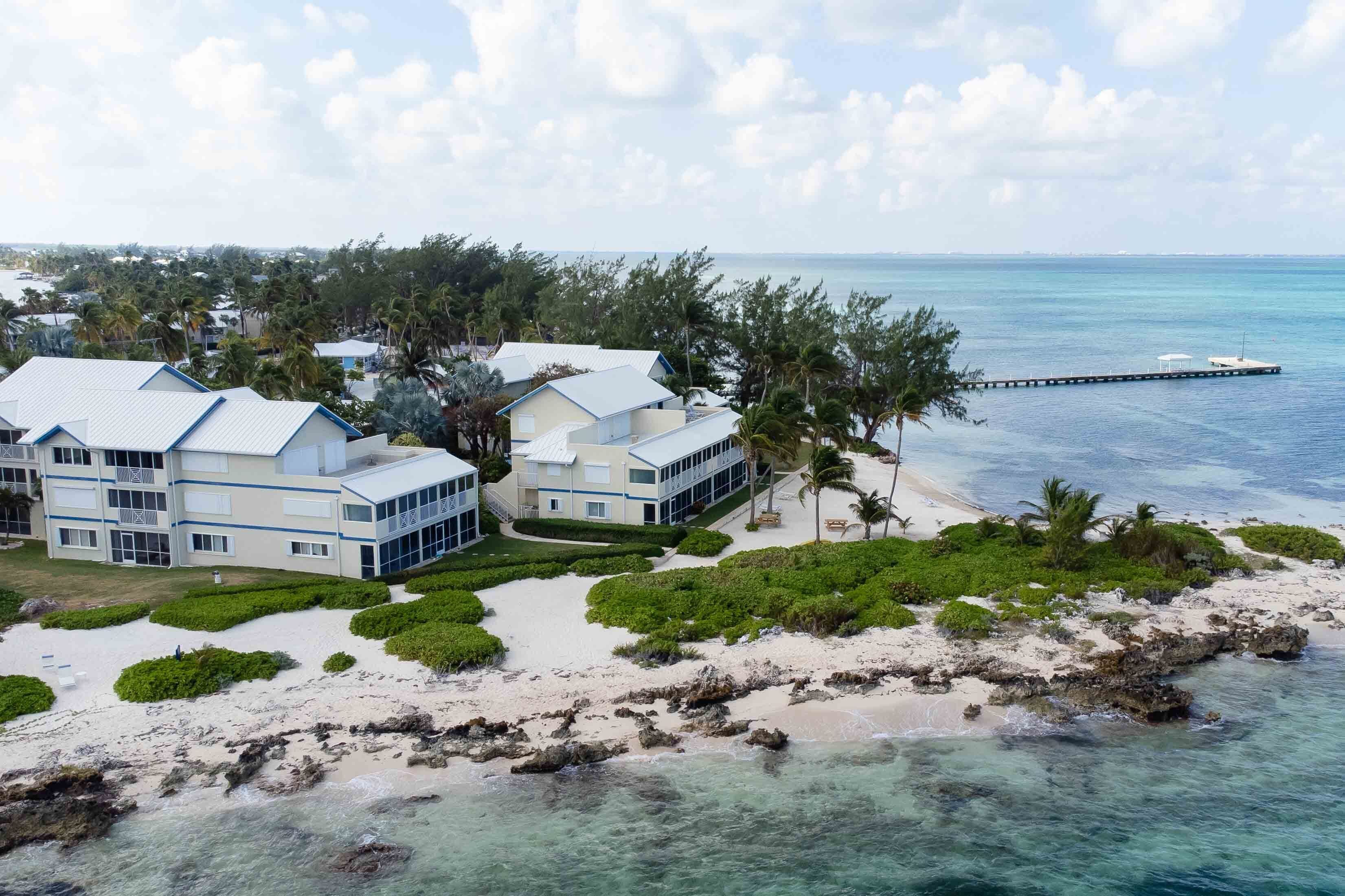 En ejendom ved stranden med flere bygninger, en mole og klart, blåt vand.