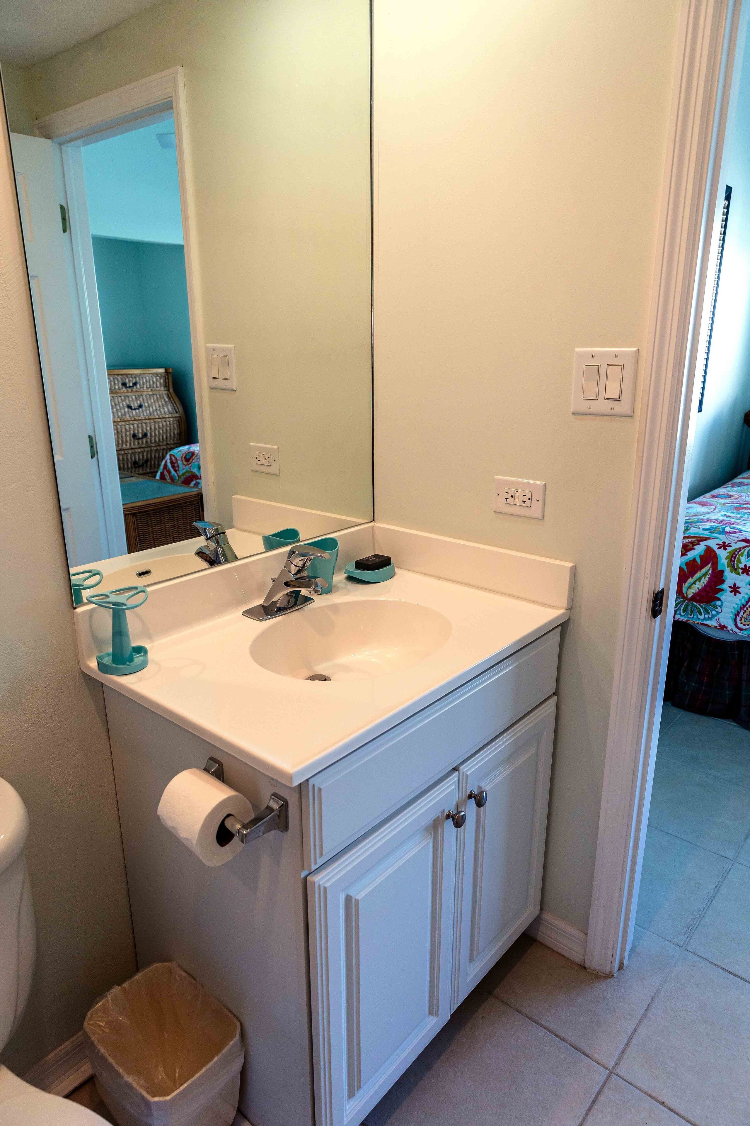 Une salle de bain avec un lavabo blanc, un miroir, des toilettes et une poubelle.