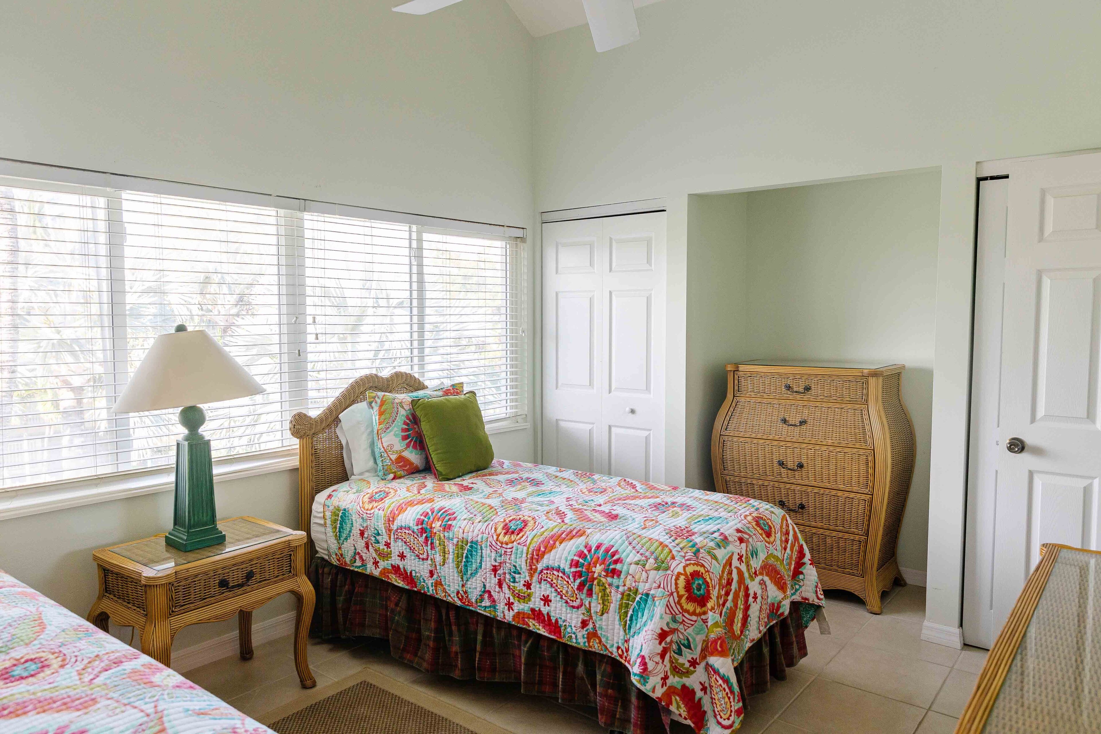 A bedroom with a bed, a dresser, a lamp, and a window with blinds.