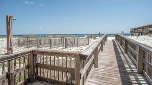 Una passerella di legno che conduce a una spiaggia con una battigia sabbiosa e un cielo azzurro terso.