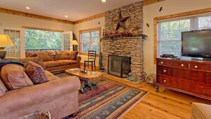 A cozy living room with a stone fireplace, a television, and a comfortable seating area. - Beautiful lodge, 4 king bedrooms, all with private baths! 5 decks to enjoy. (SKY VALLEY)