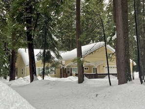 A snow-covered lodge with a large porch and tall pine trees surrounding it.