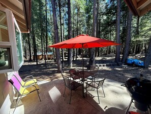 Une terrasse extérieure avec un parasol rouge, des chaises en métal et un barbecue.