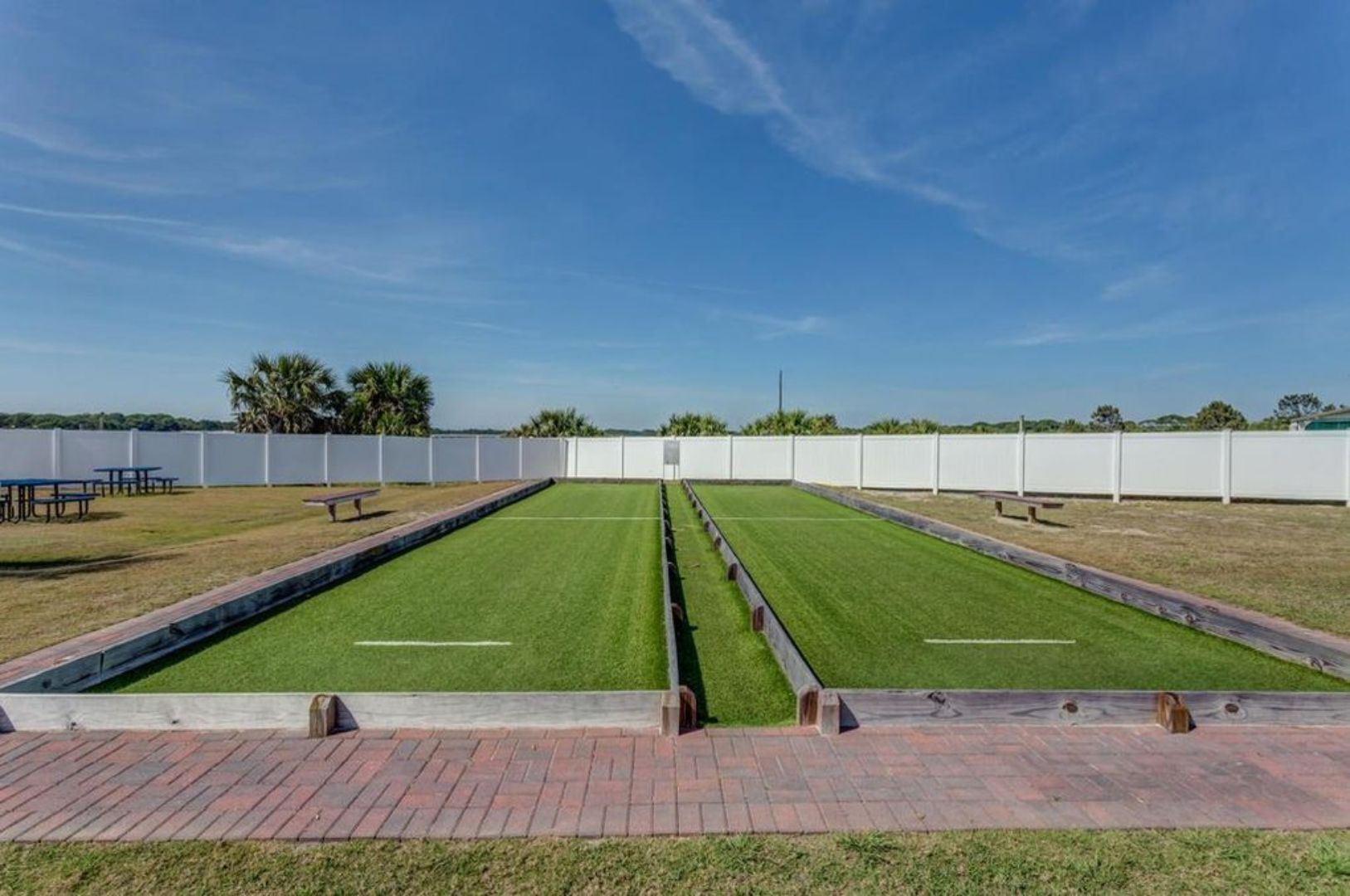 Een croquetveld met een witte omheining, groen gras en een helderblauwe lucht.