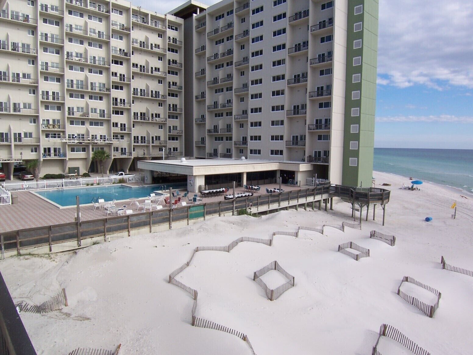 Un hotel con varios pisos, piscina y una zona de playa con tumbonas.