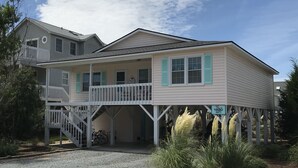 Een tweelaags huis met een balkon en een overdekte veranda, met een bord waarop staat dat het een VRBO-advertentie is.